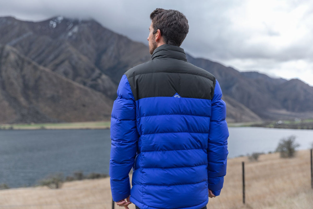 A man wearing a Kathmandu down jacket and facing a mountain range on the other side of a lake on New Zealand's South Island.