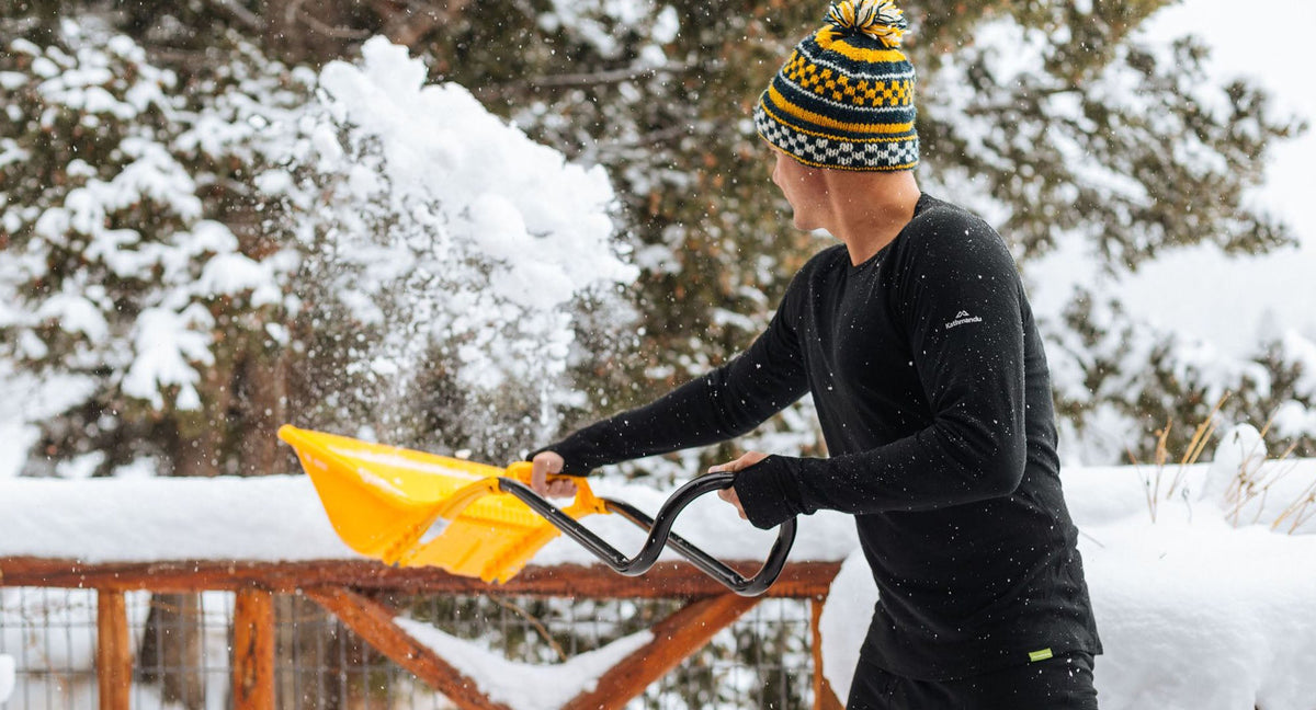 A man dressed in thermals is clearing the deck from snow in the morning.
